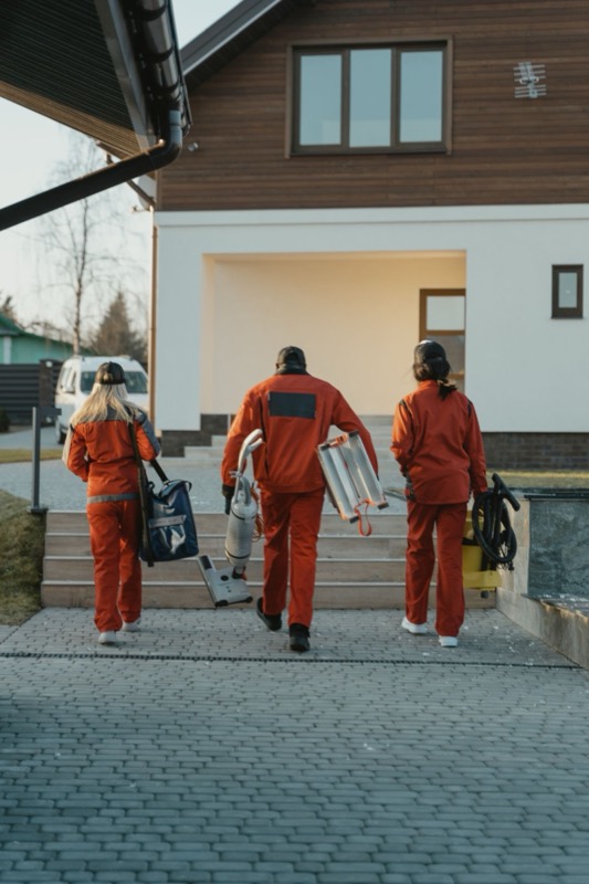 A cleaning crew in orange uniforms walking toward a house